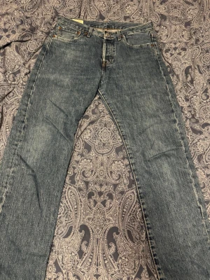 Levi's 501 blå jeans W31 L34 - Klassiska Levi's 501 jeans i blå tvätt med raka ben och femficksmodell. Slitningar vid framfickorna för en mer vintage stil