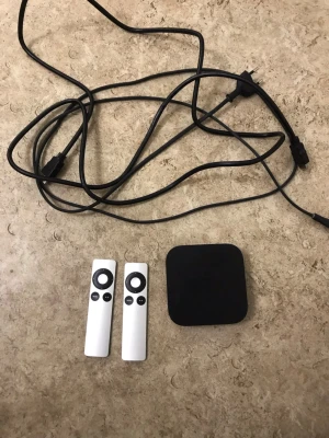 Apple TV (3rd generation) med fjärrkontroller - Apple TV (3rd gen) med två fjärrkontroller och strömkabel. Enheten har några ytliga repor och en spricka på ovansidan, men fungerar som den ska. Perfekt för streaming av filmer, serier och musik till din TV. Enkel att installera och använda.