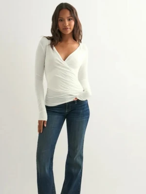 Vit omlottopp med v-ringning - Snygg vit omlottopp med djup v-ringning och långa ärmar. Toppens omlottdesign ger en smickrande siluett och den är tillverkad i ett mjukt, stretchigt material som sitter bekvämt på kroppen. Perfekt att styla med jeans eller kjol.