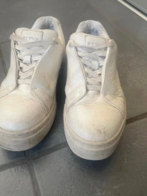Vita Eytys sneakers i skinn - Säljer ett par chunky vita sneakers från Eytys i storlek 39. Skorna har en tjock platt sula, snörning framtill och en lila rand baktill. Tillverkade i skinn med gummisula och klassisk Eytys-logga på plösen och hälen.