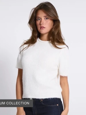 Vit stickad kortärmad topp - Superfin vit stickad topp med korta ärmar och rund hals. Den har en mjuk och fluffig känsla, ribbade kanter vid ärmslut och nederkant. Perfekt att styla med jeans eller kjol för en clean look. Orginal pris 200kr