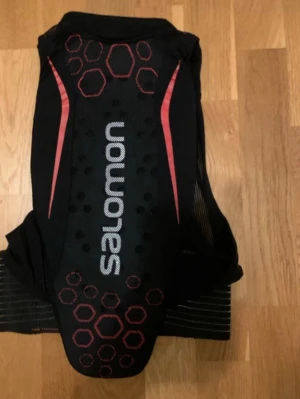 Salomon skid/snowboard ryggskydd JL - Säljer ett ryggskydd från Salomon, perfekt för skidåkning eller snowboard. Skyddet är smidigt, lätt och bekvämt att bära under jackan samtidigt som det ger bra skydd för ryggen. Ryggskyddet sitter bra mot kroppen och ger god rörelsefrihet, vilket gör det lämpligt för både pist och park. Jr large i storlek. Obs! inte samma rygskydd som andra anonsen men samma modell 