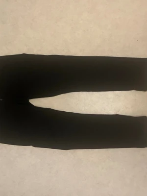 Svarta slim byxor i storlek 30/34 - Svarta byxor med slim passform, perfekta för dig som gillar en clean och stilren look. Modellen är rak och smal över benen, vilket ger en snygg siluett. Materialet känns mjukt och följsamt, och färgen är helsvart. Passar dig som vill ha ett enkelt och snyggt basplagg.