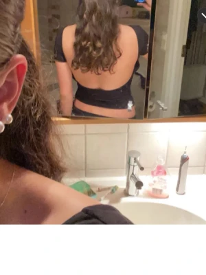 Svart topp med öppen rygg - Säljer en svart, tight topp med korta ärmar och en riktigt snygg öppen rygg. Toppen är croppad och har en stilren, enkel design som passar perfekt till jeans eller kjol. Materialet känns mjukt och stretchigt, passar både till vardag och fest!