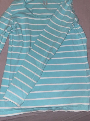 Turkos och vit randig långärmad topp - Säljer en fräsch långärmad topp från Basic U i storlek S. Toppen är turkos med vita horisontella ränder och har en rund halsringning. Perfekt att matcha med jeans eller shorts för en chill look.