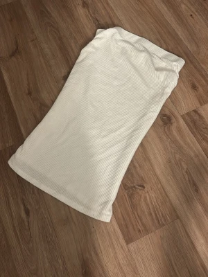 Vit kjol  från Heartbeats - Säljer en enkel och snygg vit kjol  från Heartbeats. Toppen är axelbandslös och har en mjuk, stretchig känsla som sitter skönt på kroppen. Perfekt att styla med jeans eller kjol för en clean look.