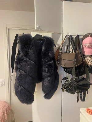 Mörkblå  pälsväst - Säljer en riktigt snygg mörkblå pälsväst med fluffig och mjuk känsla. är perfekt för att slänga över en tröja för att få en cool look. Materialet är pälsimitation och färgen är djup mörkblå. Märket är okänt.
