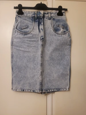 Ljusblå jeanskjol från Lee - Säljer en snygg ljusblå denimkjol från Lee med klassisk tvättad look. Kjolen har fickor fram och bak, bälteshällor och en cool patch på bakfickan. Slits med dragkedja bak för extra edge. Perfekt till sneakers eller boots!