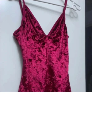 Vinröd sammetstopp med smala axelband - Säljer en vinröd bodysuit i mjuk sammet med smala axelband och v-ringad hals. Toppen har en tight passform och är ärmlös, vilket gör den riktigt snygg till både jeans och kjol. Perfekt för dig som gillar att sticka ut med färg och material.