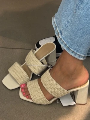 Beige sandaler med breda band - Säljer ett par stilrena beige sandaler med två breda, flätade band över foten och fyrkantig tå. Perfekta för varma dagar och har en öppen design som visar tårna. Passar dig som gillar minimalistisk och trendig stil. Beige klackskor med blockklack och fyrkantig tå från hm. Endast använda en gång. Väldigt bekväma. Flätat material