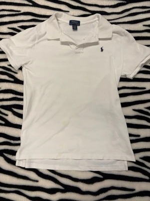 Ralph Lauren Piké - Vit piké från Polo Ralph Lauren. Den har 1 defekt vilket man ser sista bilden där det är 3 små fläckar. Storleken är i kids XL (18-20) vilket blir S i vuxen. Hör av dig vid minsta fundering 😀 