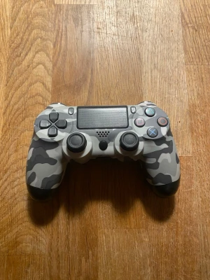 PlayStation 4 DualShock 4 Camo Edition - Snygg DualShock 4 handkontroll till PlayStation 4 i grå kamouflage-design. Kontrollen har touchpad, inbyggd högtalare och klassiska PS-knappar.  Säljer för att jag inte har ngn andvändning av  kontrollen och för att jag har fått nya kontroller. För fingering måste en laddning sladd sitta i kontrollen!