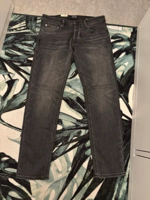 Svarta jeans från Jack & Jones W32 L32 - Säljer ett par svarta jeans från Jack & Jones med klassisk femficksdesign och diskret tvättad look. Jeansen har rak passform och är tillverkade i mjukt bomullsmaterial med lite stretch för extra komfort. Perfekt för dig som gillar stilrena och enkla jeans. Köpta för 1099 