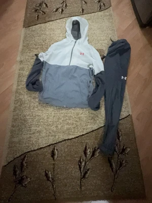 Under armour tracksuit  - Bilderna visar en träningsjacka och ett par träningsbyxor från Under Armour i grått och vitt,