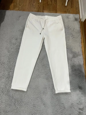 Vita slim fit mjukisbyxor LCW Vision - Fräscha vita mjukisbyxor från LCW Vision i storlek L. Slim fit-modell med elastisk midja och snörning framtill. Byxorna har fickor på sidorna och bak, och är gjorda i mjukt bomullsmaterial som är skönt mot huden. Perfekt för chill dagar eller när du vill vara extra bekväm.