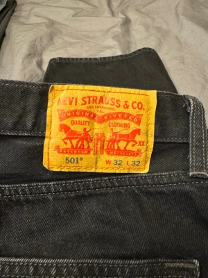Levi's 501 svarta jeans W32 L32 - Svarta Levi's 501 jeans med klassisk rak passform och fem fickor. Jeansen har en ikonisk läderpatch bak i midjan och är tillverkade i slitstarkt bomullsdenim. Perfekta för dig som gillar tidlös stil och vill ha ett par jeans som funkar till allt.