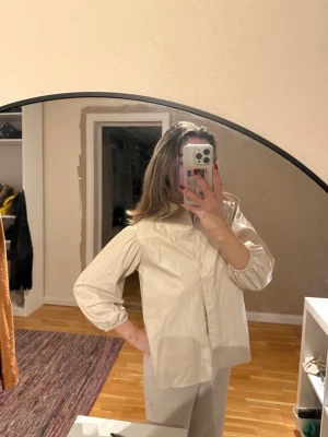 Beige skjorta i skinnimitation från Lindex - Säljer en beige skjorta i skinnimitation från Lindex. Skjortan har klassisk krage, knäppning framtill och ballongärmar med resår vid ärmslut. 