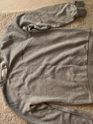 Grå sweatshirt från Henri Lloyd - Säljer en enkel och stilren grå sweatshirt från Henri Lloyd i storlek L. Tröjan har rund hals, långa ärmar och ett diskret svart tryck med logga på bröstet. Perfekt för chill dagar och passar till jeans eller mjukisbyxor.