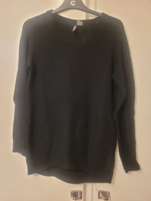 Svart stickad tröja från H&M Divided - Svart stickad tröja från H&M Divided i storlek XS. Tröjan har rund halsringning och långa ärmar, med en enkel och klassisk design. Perfekt för att hålla sig varm under kyliga dagar och passar till många olika stilar.