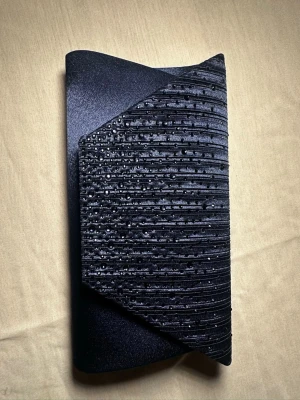 Marinblå kuvertväska med paljettdetaljer - Snygg marinblå kuvertväska i satin med glittriga paljetter på framsidan och ett coolt veckat mönster. Väskan har en stilren och modern form, perfekt att hålla i handen. Materialet är mjukt och har en lyxig känsla.