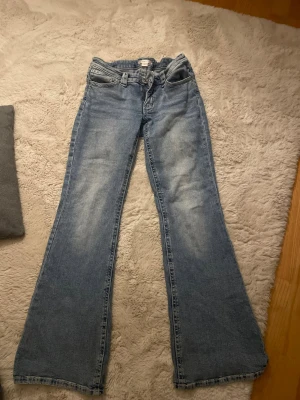 Bootcut jeans från Gina Tricot - Snygga bootcut jeans från Gina Tricot i ljusblå tvätt med slitningar och coola detaljer på bakfickorna. Klassisk femficksmodell med knapp och dragkedja framtill. Perfekt för dig som gillar retrovibbar och breda ben.