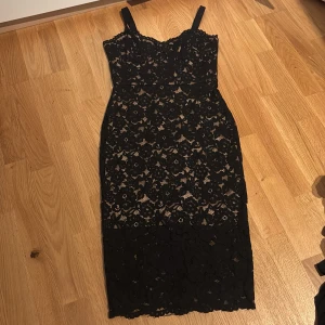 Svart spetsklänning med beige foder - Supersnygg svart spetsklänning med beige foder och smala axelband. Klänningen har figurnära passform, blommigt spetsmönster och dragkedja i sidan. Perfekt för dig som vill sticka ut med en elegant och feminin look. Prislapp sitter kvar