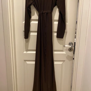 Brun långklänning med snörning - Säljer en brun abaya, köpt i Köpenhamn. Har en snörning i mitten så den kan tajtas till och därmed passar alla storlekar. 