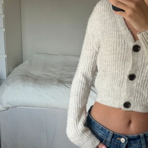 Beige croppad kofta från H&M - Supermysig beige stickad kofta från H&M med croppad passform och bruna knappar framtill. Tröjan har v-ringning och långa ärmar, barnstorlek men sitter snyggt ändå😊💕