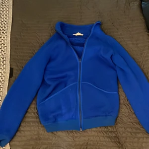 Blå fleecejacka från Helly Hansen - Säljer en blå fleecejacka från Helly Hansen med hel dragkedja och höga fickor framtill. Jackan är tillverkad i 100% polyester och har en klassisk, sportig look med lång ärm och ståkrage. Perfekt för kyliga dagar och outdoor-häng.