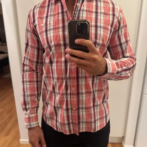 Orange och vit rutig skjorta - Snygg rutig skjorta i orange, vitt och blått med klassisk krage och knäppning framtill. Skjortan har lång ärm och en bröstficka med knapp. Perfekt för dig som gillar en färgstark och stilren look.