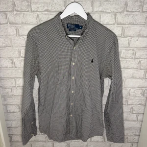 Ralph Lauren skjorta - Snygg svartvit rutig skjorta från Ralph Lauren i slim fit-modell. Skjortan har klassisk krage, knäppning framtill och broderad logga på bröstet.  Användbar till det mesta - både jeans och chinos funkar perfekt! Hör av dig vid intresse 🙌