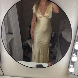 Ljusgul långklänning från Hello Molly - Supersnygg ljusgul långklänning från Hello Molly i glansigt satinliknande material. Klänningen har djup v-ringning, korta ärmar och en öppen rygg med snygg cut-out detalj. Figurnära passform. Helt ny! Därav priset. OBS! Ligger uppe på min vinted också! 