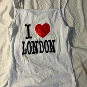 Vit linne-topp med I Love London-tryck - Vit linne-topp med tunna axelband och tryck i svart och rött där det står 'I ❤️ LONDON' på framsidan. Perfekt för dig som älskar London och vill ha en enkel men uttrycksfull topp till sommaren.