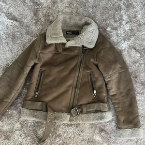 Mysig höstjacka  - Snygg brun höstjacka från Zara med   mysigt teddy foder. Jackan har dragkedja i sned modell, två fickor med dragkedja och bälte i midjan. Perfekt för kyliga dagar och ger en cool look till alla outfits. Endast använd vid ett tillfälle då jag skulle ha jackan till en outfit ☺️ 