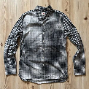 Rutig skjorta från Levi's i bomull - S - Snygg rutig skjorta från Levi's i svart och vitt. Skjortan har klassisk krage, knäppning framtill och en bröstficka. Tillverkad i mjuk bomull och har långa ärmar med knappar vid manschetterna. Perfekt för en avslappnad och stilren look.