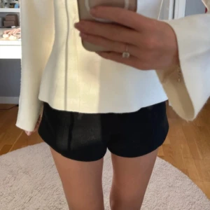 Svarta kostymshorts - Snygga svarta kostymshorts med hög midja och stilren passform. De har en enkel design utan synliga detaljer och är gjorda i ett mjukt, lite tjockare material som ger en clean look. Perfekta för dig som gillar minimalistisk stil och vill ha ett par shorts som sitter bra. Materialet är lite stickat.