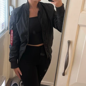 Svart bomberjacka Alpha Industries S - Säljer en svart bomberjacka från Alpha Industries i storlek S. Jackan har orange insida, ribbade muddar och dragkedja framtill. På ärmen finns en ficka med röd tagg. Använd varsamt och inga har inga fel.