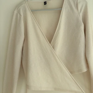 Beige omlottopp från H&M - En beige ribbad omlottopp från H&M med lång ärm och djup v-ringning. Toppen har knytband i midjan. Skriv om du har frågor💗