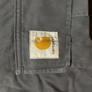 Mörkblå cargobyxor från Carhartt - Säljer ett par mörkblå cargobyxor från Carhartt med klassisk logga på benet. Byxorna har flera stora fickor på sidorna och är tillverkade i slitstark bomull. Perfekta för dig som gillar streetwear och praktiska detaljer.