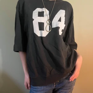 Svart loose sweatshirt - Svart sweatshirt med stort vitt tryck '84' på framsidan. Modellen är loose fit med breda, lite längre korta ärmar och rund halsringning. Materialet känns som mjuk bomull, perfekt för en chill och avslappnad stil.