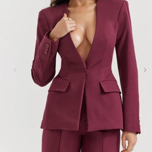 Vinröd kavaj från House of CB - Snygg vinröd kavaj från House of CB med djup v-ringning och figurnära passform. Kavajen har långa ärmar, markerad midja, två fickor med lock och knappar vid ärmslut. Perfekt för dig som vill sticka ut med en stilren och modern look. Storlek medium men passar mig som är S. 