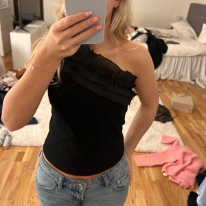 Svart oneshoulder topp med volang - Snygg topp från studio eleven 💞dock hål på ena sidan men går lätt att sy ihop, men ser även en vit tråd på framsidan men inget man tänker på kolla bild för att se defekter 💞💞därför säljs den billigt 😊