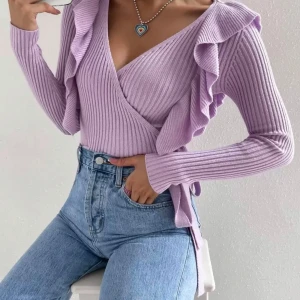 Ljuslila omlottopp med volangdetaljer - Superfin ljuslila omlottopp i ribbad stickad kvalitet. Toppen har långa ärmar, v-ringning och snygga volanger längs axlarna. Knytband i midjan för en extra snygg passform. Perfekt att styla med jeans eller kjol för en trendig look.