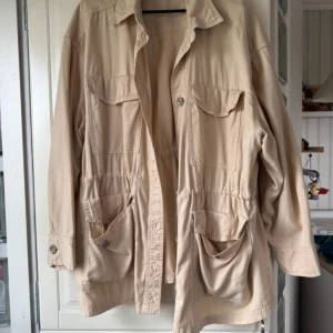 Beige utilityjacka med stora fickor - Snygg beige utilityjacka med fyra stora fickor framtill och knappar. Jackan har dragsko i midjan för en schysst passform och klassisk krage. Perfekt för lager-på-lager och enkel att styla till det mesta.
