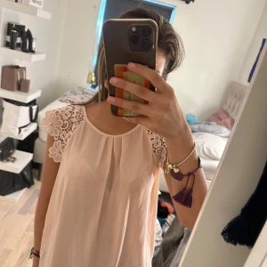 Ljusrosa klänning med spetsdetaljer - Supersöt ljusrosa klänning med vackra spetsdetaljer på axlarna och rund halsringning. Klänningen har en lös passform och är ärmlös, perfekt för varma dagar. Stilren och feminin look som passar till många tillfällen.