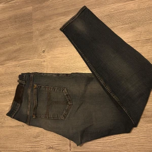 Mörkblå  jeans från Tiger of Sweden - Säljer ett par mörkblå  jeans från Tiger of Sweden med klassisk femficksdesign och snygga slitningar på benen. Jeansen har kontrastsömmar och en läderpatch bak i midjan. Perfekta för dig som gillar en tight passform och stilren look.