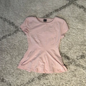 Ljusrosa topp från Gina Tricot XS - Supersöt ljusrosa topp från Gina Tricot i figurnära modell med korta ärmar och rund halsringning. Toppen har en lätt utsvängd nederdel och är tillverkad i mjuk bomull, perfekt för en fräsch och enkel look.