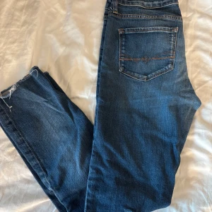 Blå jeans från Tommy Hilfiger - Snygga blå jeans från Tommy Hilfiger med klassisk femficksdesign och råa, avklippta benslut. Jeansen har en normal passform och är tillverkade i mjukt bomullsjeans med lätt tvättad look och kontrastsömmar.