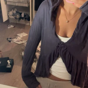 Mörkblå omlottkofta med volang - Säljer en mörklila omlottkofta från H&M med volangdetalj framtill och långa ärmar. Koftan har en snygg knytning framtill och är tillverkad i mjuk bomull, perfekt för lager-på-lager och chill outfits.