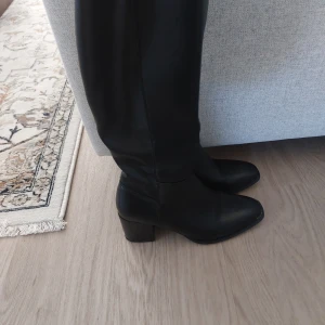 Svarta stövlar med klack och dragkedja - Snygga svarta stövlar i skinnimitation med medelhög klack.. Stövlarna har dragkedja på insidan för enkel påtagning och en stilren, minimalistisk look. Perfekta till jeans eller kjol för en trendig vibe.Det finns en liten skada uppe på en stövel.Kolla bilder.